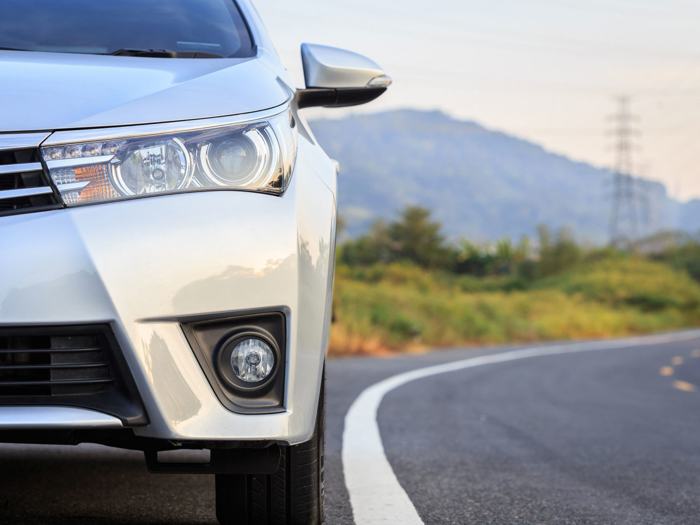 Close up front of silver car on road with hills in the background