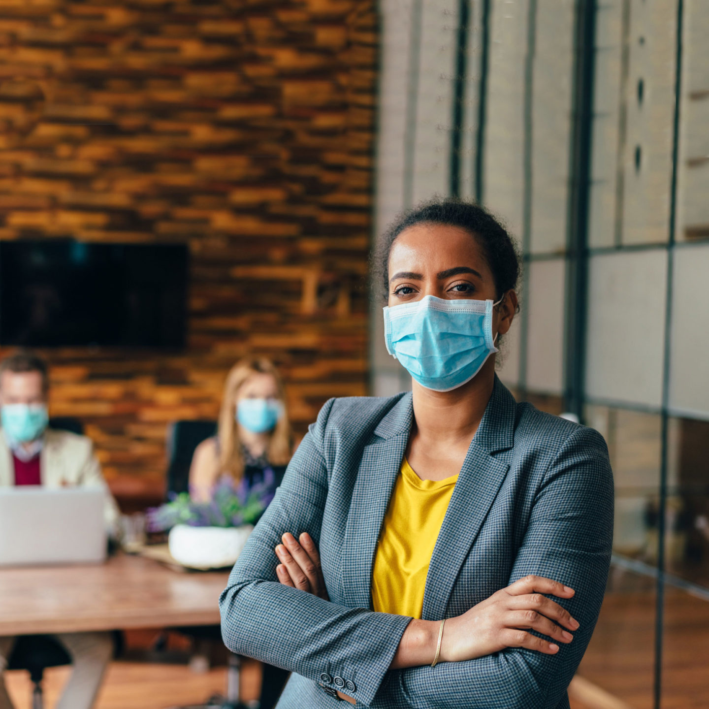 Business people masks in an office with businesswoman looking at camera