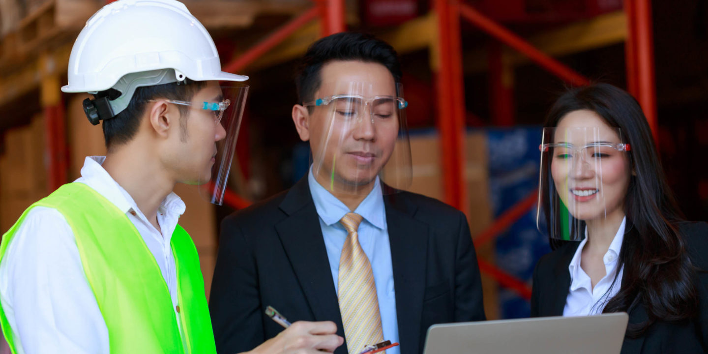 Business man and woman talking to construction worker while wearing face shields