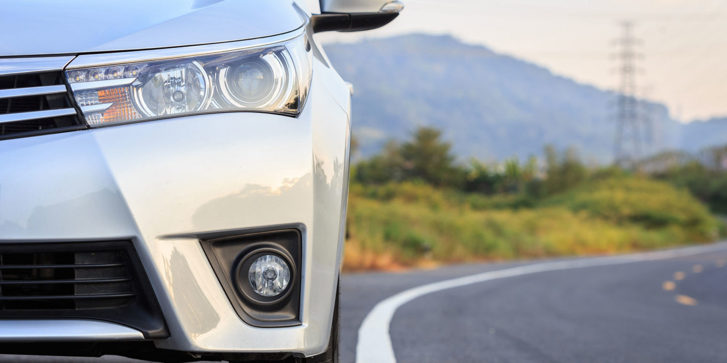 Close up front of silver car on road with hills in the background