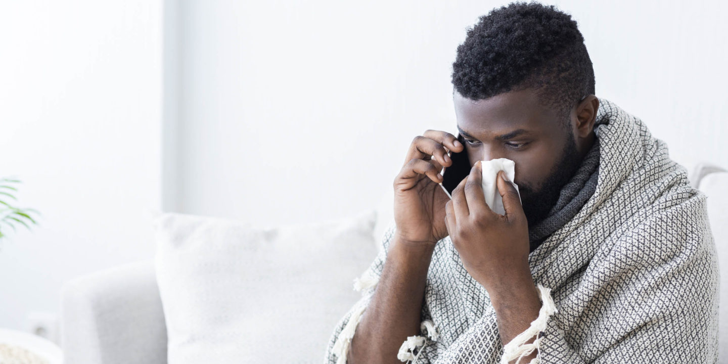 Man on phone with tissue covering his nose - Be a Flu Fighter: Protect Yourself From the Flu | NSF International