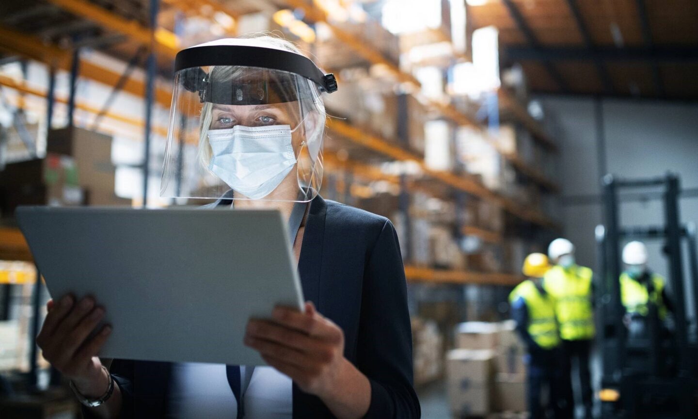 Woman on tablet in warehouse wearing mask | NSF International