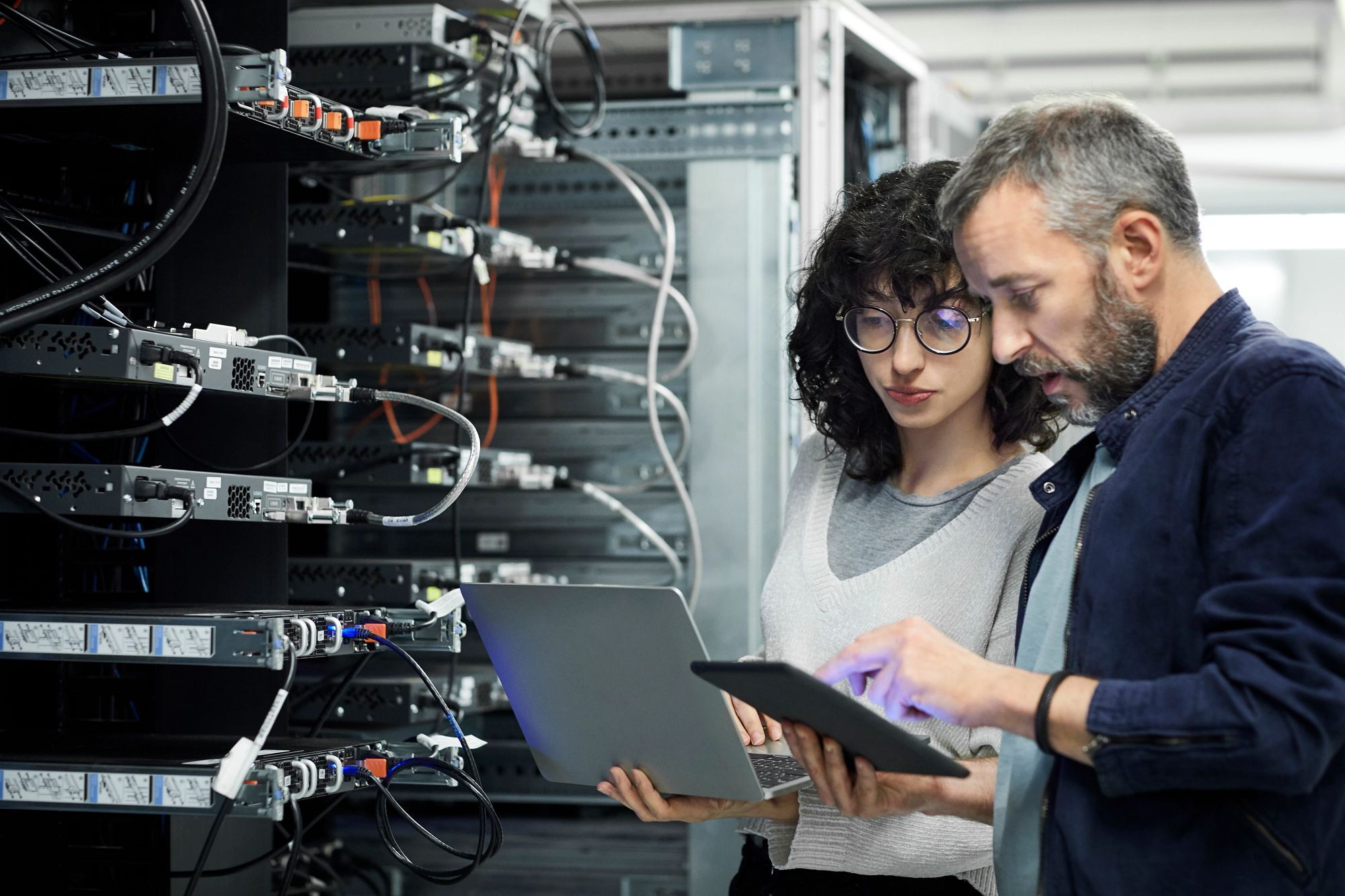 Two people in a server room reviewing information on a laptop and tablet - Celebrating 80 Years of Improving Human and Planet Health | NSF