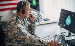 American soldier sitting in headquarters office wearing a headset while using a computer - Cybersecurity Maturity Model Certification (CMMC) | NSF